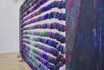 Das Kunstwerk steht quer im Raum. An einem Netz wurden von beiden Seiten kleine Gesichter aufgehängt - in mehreren Reihen, vertikal, wie horizontal. Sie haben alle unterschiedliche Farben, die sich aber in Abstufungen einander gleichen. Das Farbspektrum bewegt sich zwischen Blau, Violett und Grün.