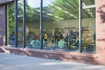 Die Fensterfront des ICAT-Ausstellungsraumes zeigt den Titel der Ausstellung in schwarzer und gelber Schrift. Im Innenraum sind viele Menschen zu erkennen.