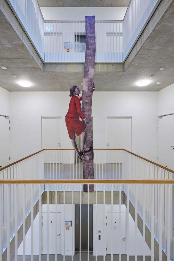 Die Darstellung einer Frau klettert an einem Baumstamm hinauf. Das Werk ist ein Cutout, das hochkant in der Galerie des AtelierHauses angebracht wurde.