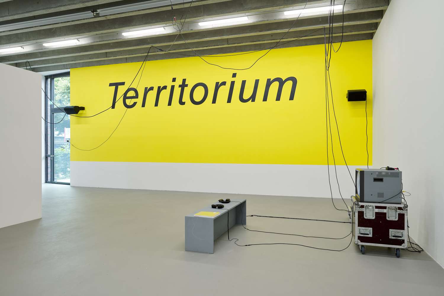 Eine große Wand wurde gelb gestrichen und darauf in großen Lettern geplottet: Territorium. Es hängen diverse Kabel unter der Decke des Raumes.