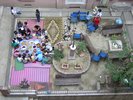 From the bird's eye view you can see a square, which is covered with various carpets. In the left half of the picture, people are grouped around a table with a blue tablecloth. On the table are bowls with food.