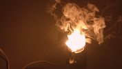 Das Still zeigt eine Lampe die raucht vor Hitze. Das Licht selbst ist weiß ausgebrannt der Rauch um die Lichtquelle herum ist warm orange.