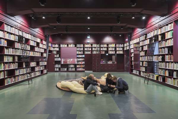 Der Bibliotheksraum wird von Studierenden als Aufenthaltsraum genutzt. Die Wände sind durch Bücherregale definiert. An der rückläufigen Wand ist ein Servicetresen zu sehen.