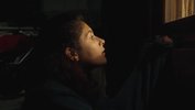 Es ist dunkel, ein Mädchen schaut in ein leuchtendes Fenster, sie hält sich am Fensterrahmen fest. Im Hintergrund ist ein Moped zu erahnen.