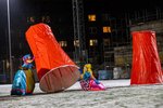 Übergroße rote Plastikbecher werden von zwei stark kostümierten Personen auf einem schneebedeckten Sportfeld bewegt