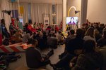 Eine Gruppe von Besucher*innen sitzt auf dem Boden in Klassenraum und lauscht einem Vortrag