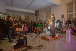 Menschen sitzen auf dem Boden und hören einer Person zu, die am Mikro steht und etwas vorliest