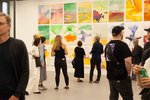 Besucher:innen stehen im Ausstellungsraum des AtelierHauses vor einer mit Gemälden behängten Wand. Die Bilder zeigen farbenfrohe Abstraktionen. Die Künstlerin ist Olga Moș.