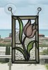 Ein flaches Glasobjekt in Form einer Tulpe hängt mit Saugnäpfen befestigt an einem Fenster. Draußen ist das Meer zu sehen.