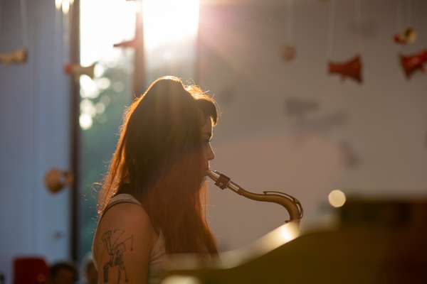 Eine Saxophon spielende Frau wird gegen die untergehende Sonne abgebildet.