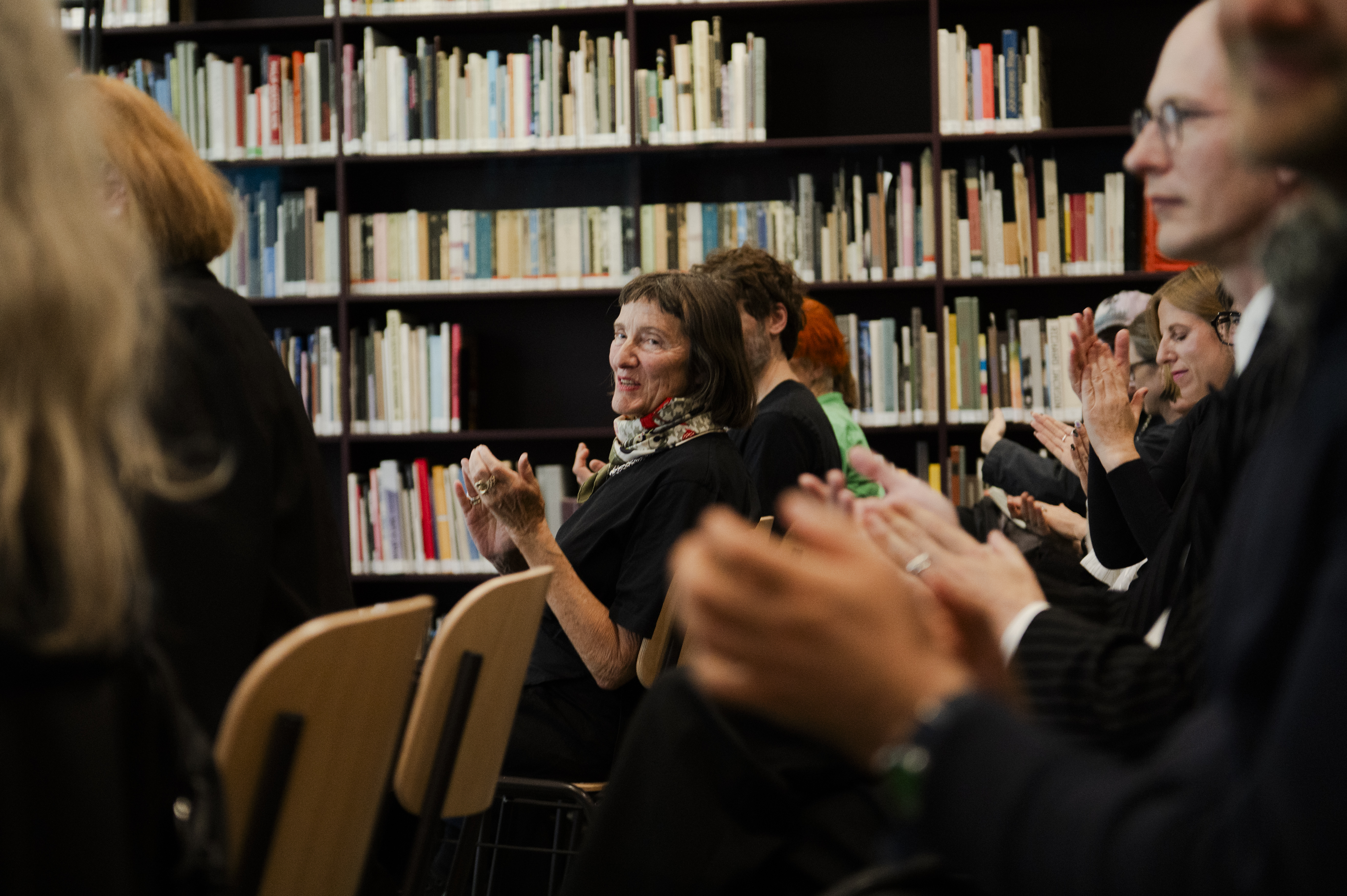 Publikum applaudiert während einer Buchpräsentation in der Extended Library der HFBK Hamburg. Im Hintergrund füllen Bücherregale den Raum.