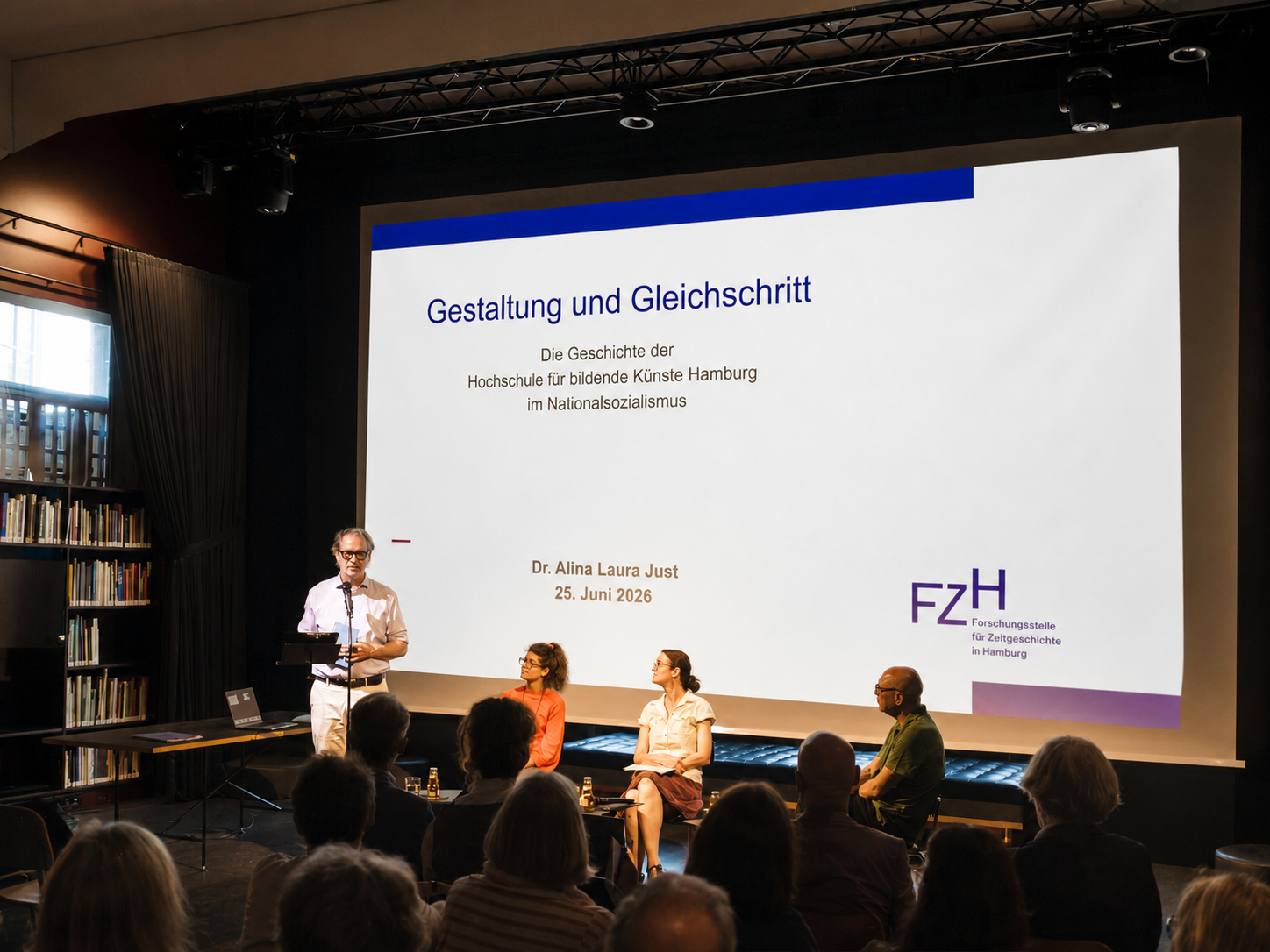 Vortrag von Dr. Alina Laura Just zur Präsentation ihrer Studie „Gestaltung und Gleichschritt. Die Geschichte der Hochschule für bildende Künste Hamburg im Nationalsozialismus“ in der Extended Library der HFBK Hamburg. Im Vordergrund sitzt das Publikum, auf der Bühne diskutieren mehrere Teilnehmende vor einer großformatigen Projektion des Vortragstitels.