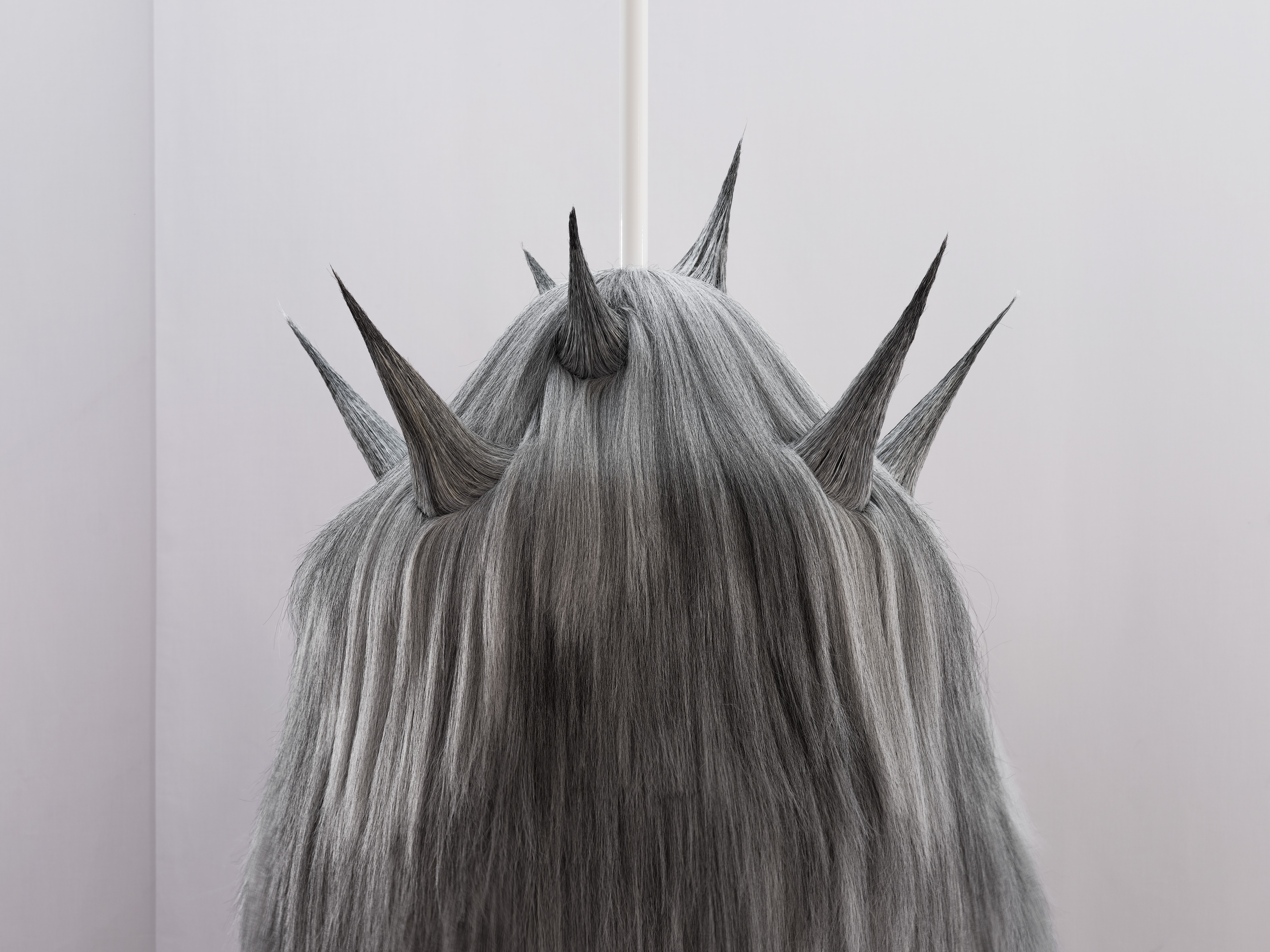 Detail view of a sculpture made of long grey hair, with several pointed, horn-like forms protruding from its surface.