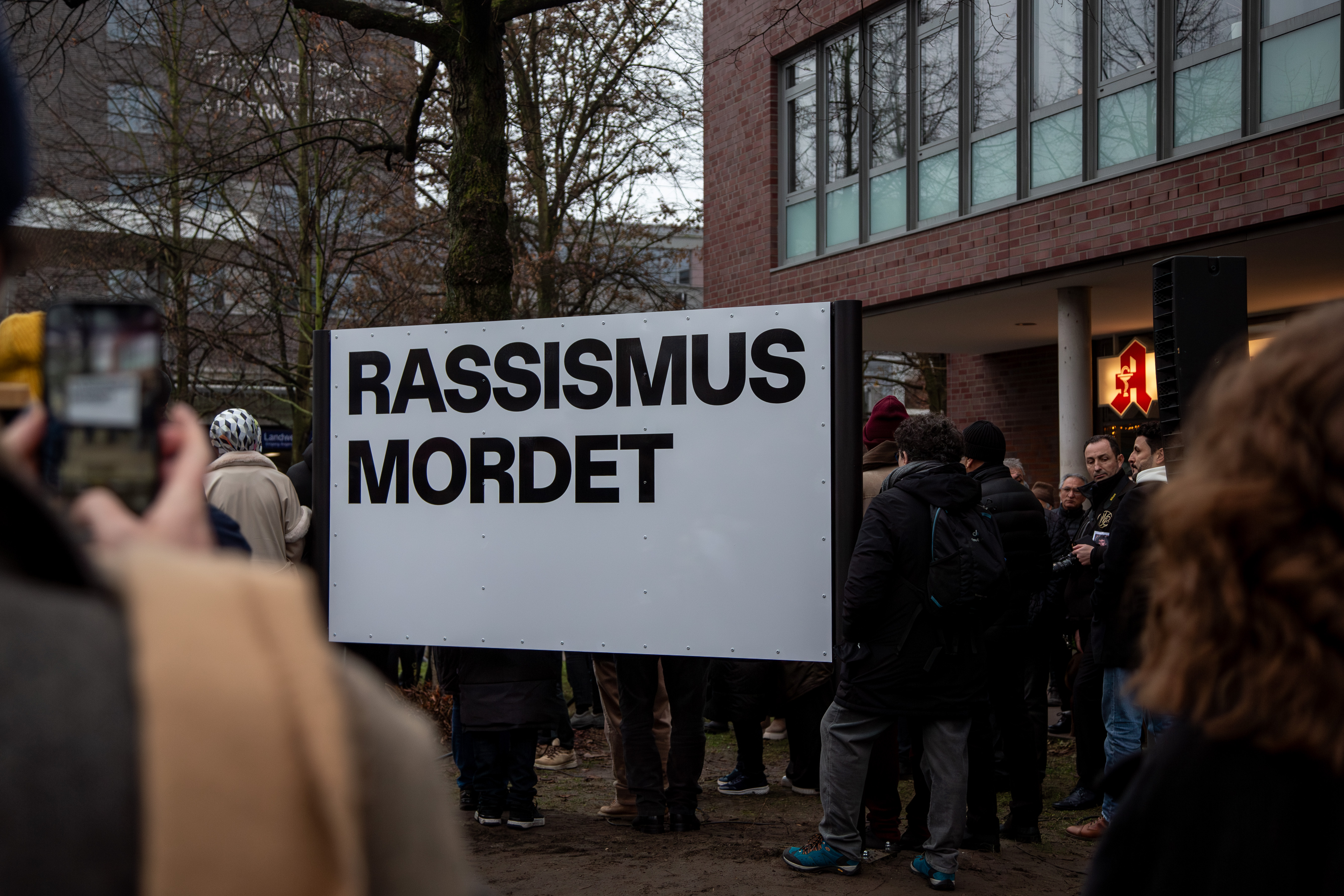 Mehrere Menschen stehen um eine Schild auf Stehlen mit der Aufschrift "Rassismus tötet".