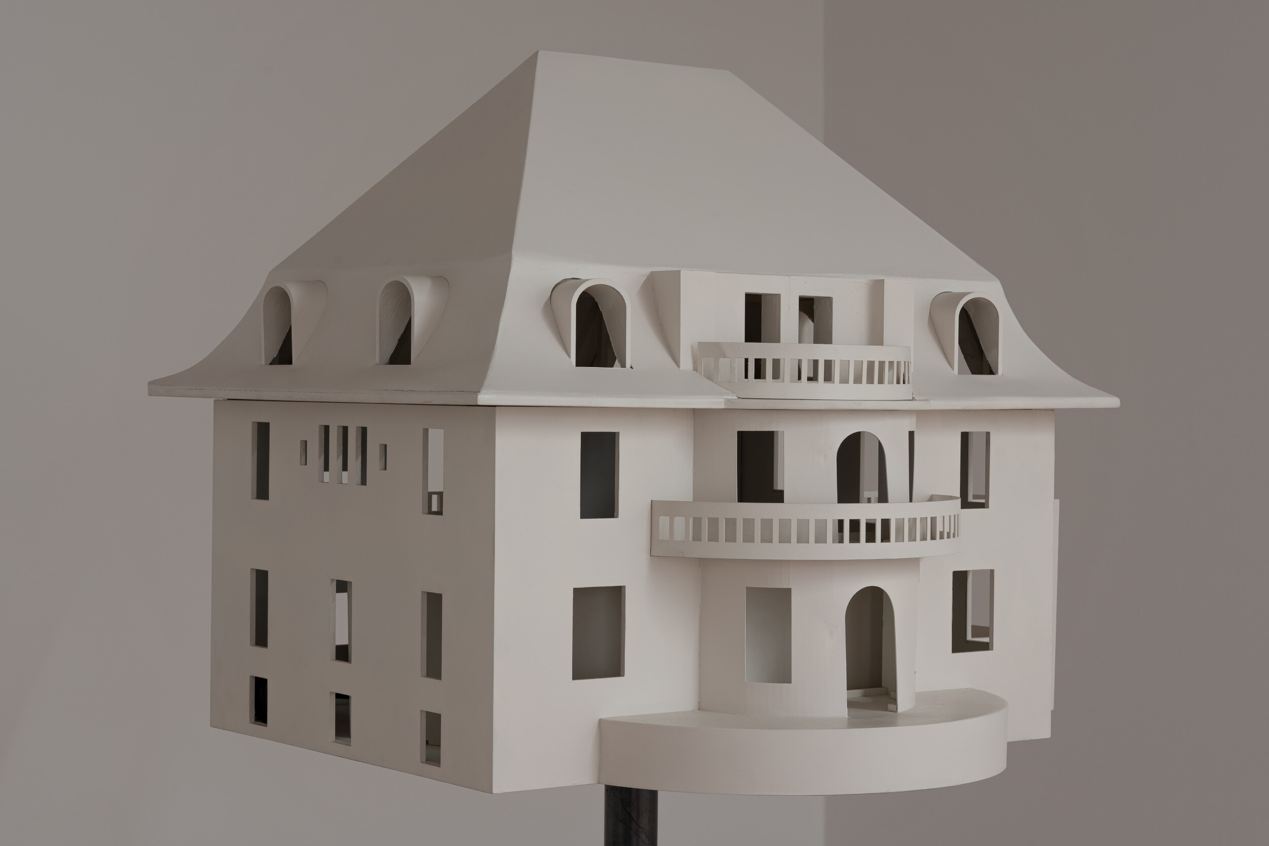 Architekturmodell eines mehrstöckigen Gebäudes aus weißem Material mit Balkonen, Rundbögen und einem geneigten Dach.