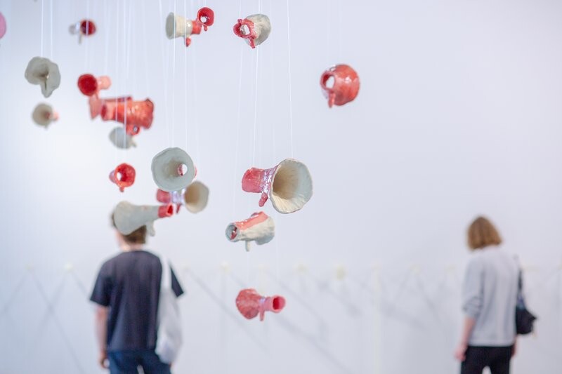 Ceramic megaphones hang from strings in the room.