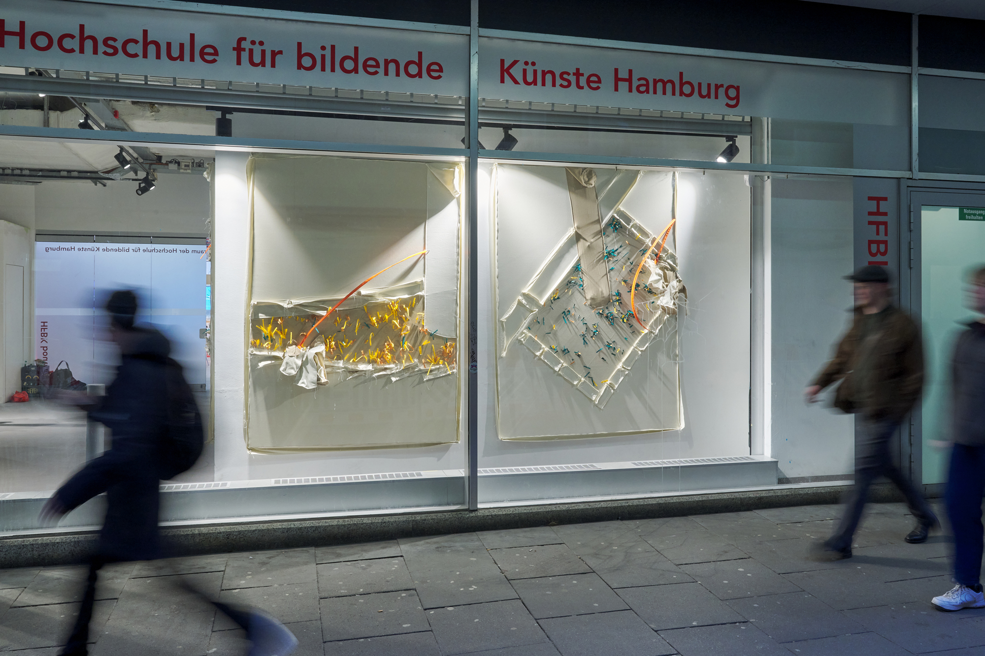 People walk past the HFBK Boutique, where two large abstract artworks are displayed in a brightly lit window.