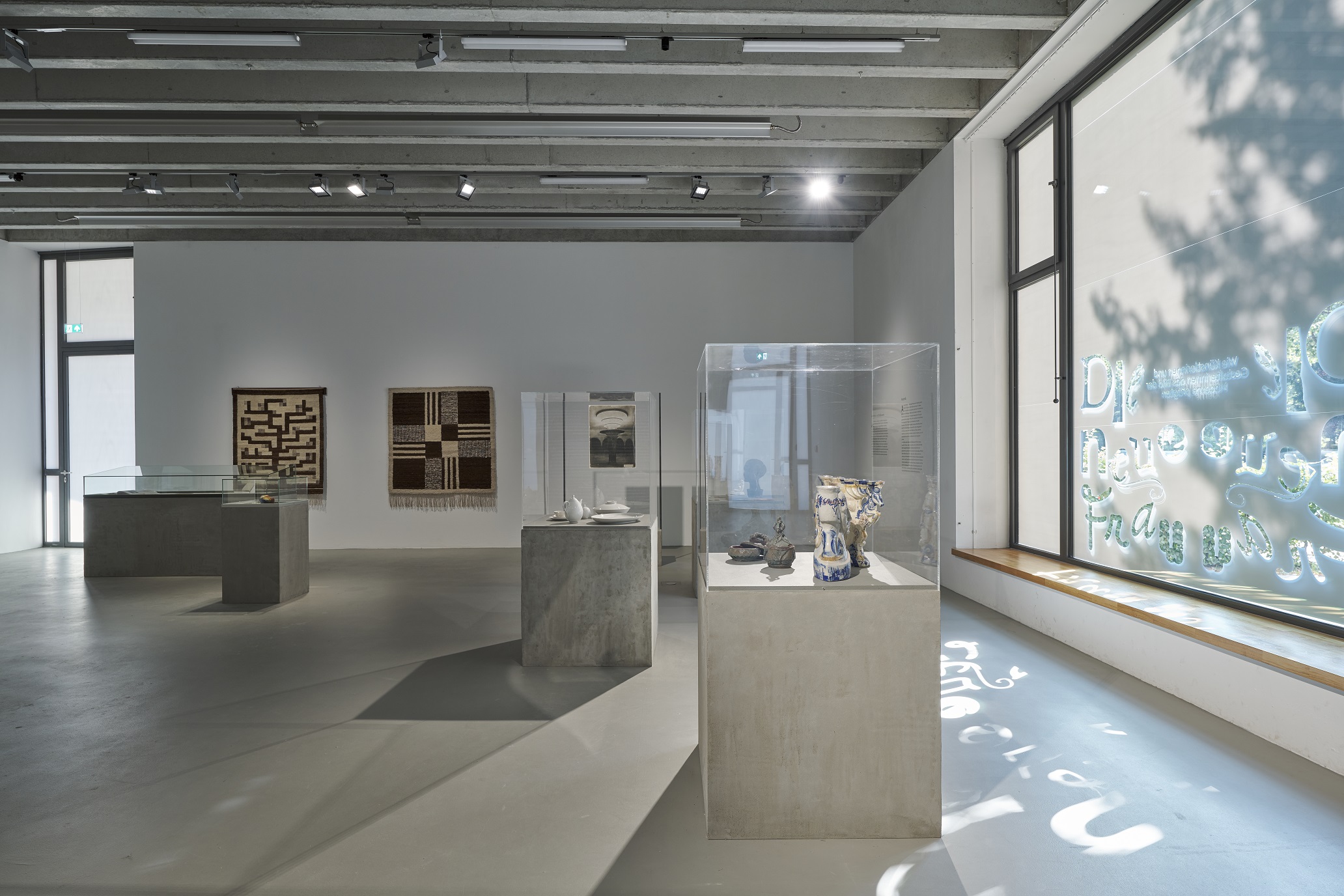 Ausstellungsstücke in Vitrinen und Wandteppiche im Hintergrund in minimalistischer Architektur.