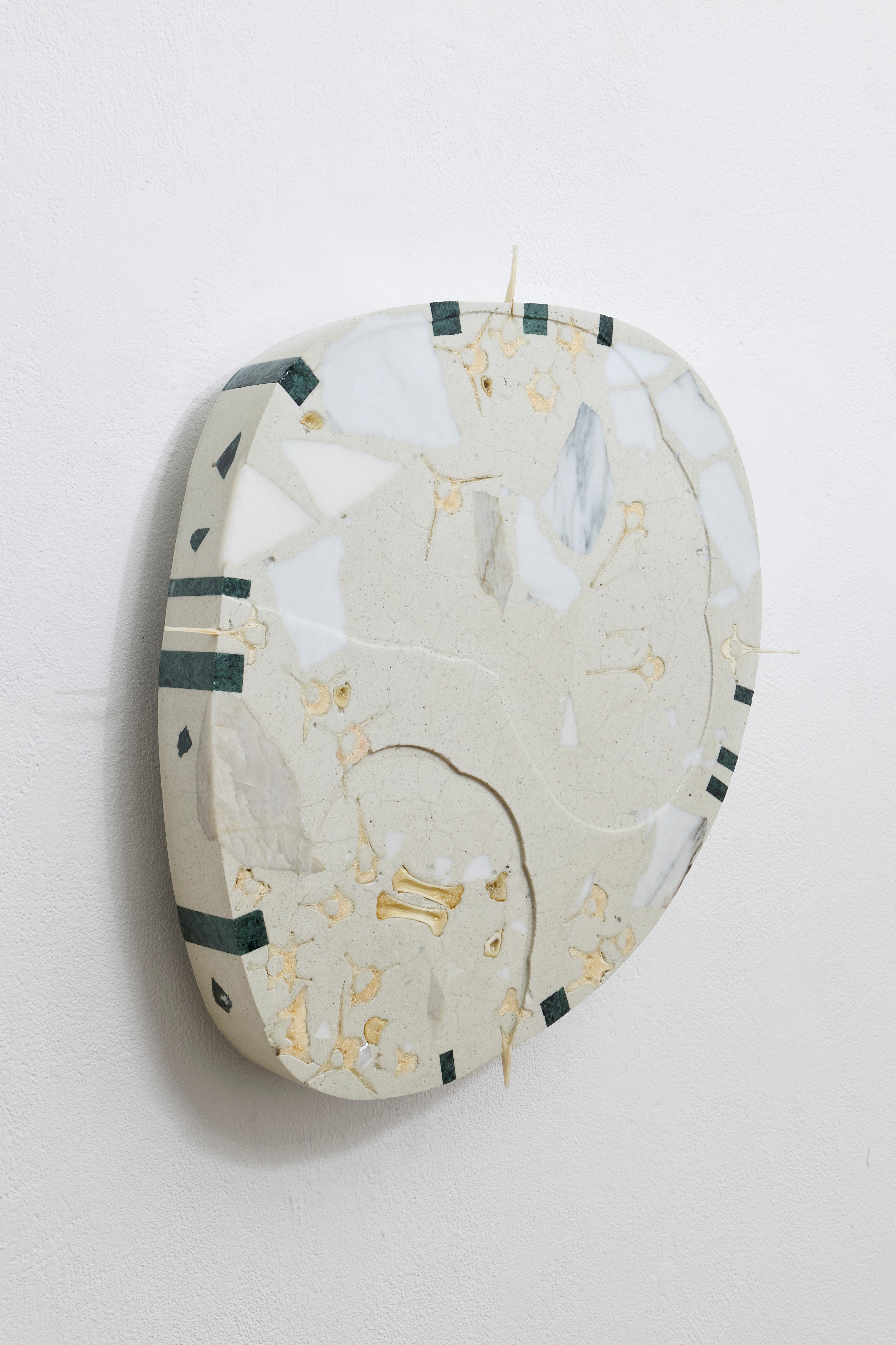 Irregularly shaped flat object with light and dark marble or stone patterns hanging on a white wall.