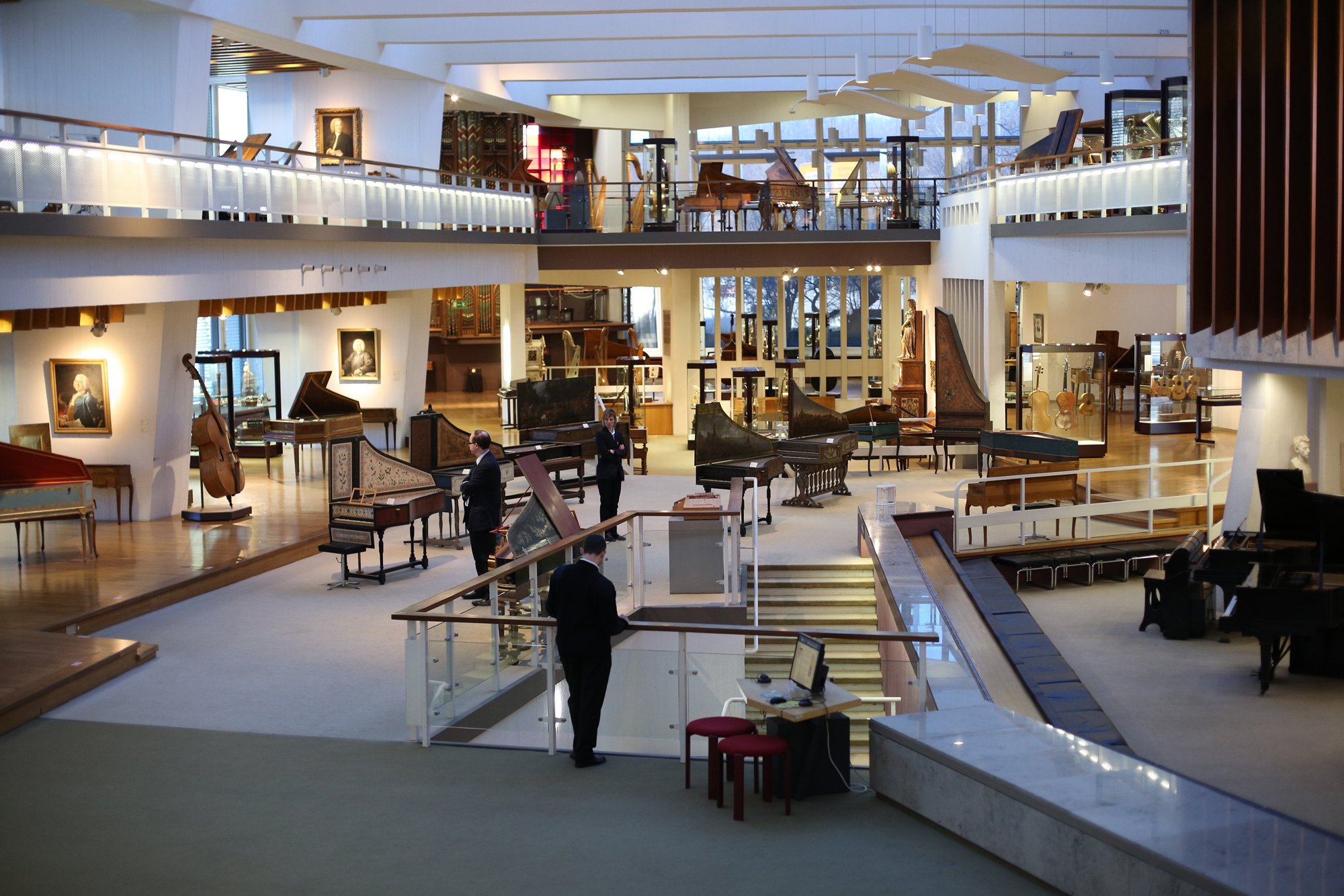 Wide-angle view of a museum featuring numerous historic keyboard and string instruments, with several visitors in the exhibition area.