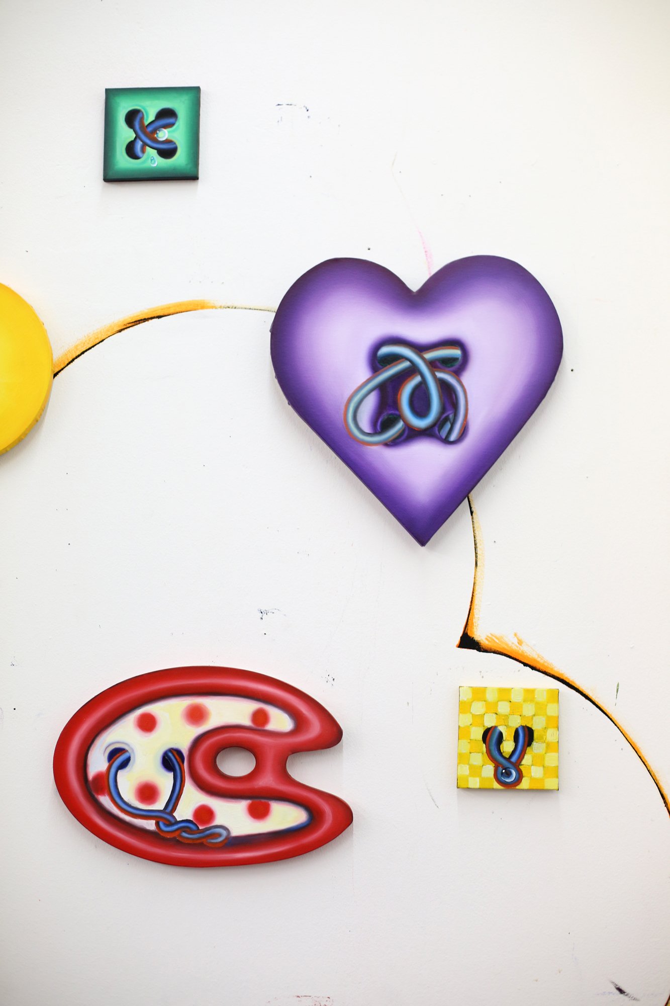 Several colorful wall objects in various shapes, including a purple heart, a red-white form, and small square panels, are mounted on a white wall.