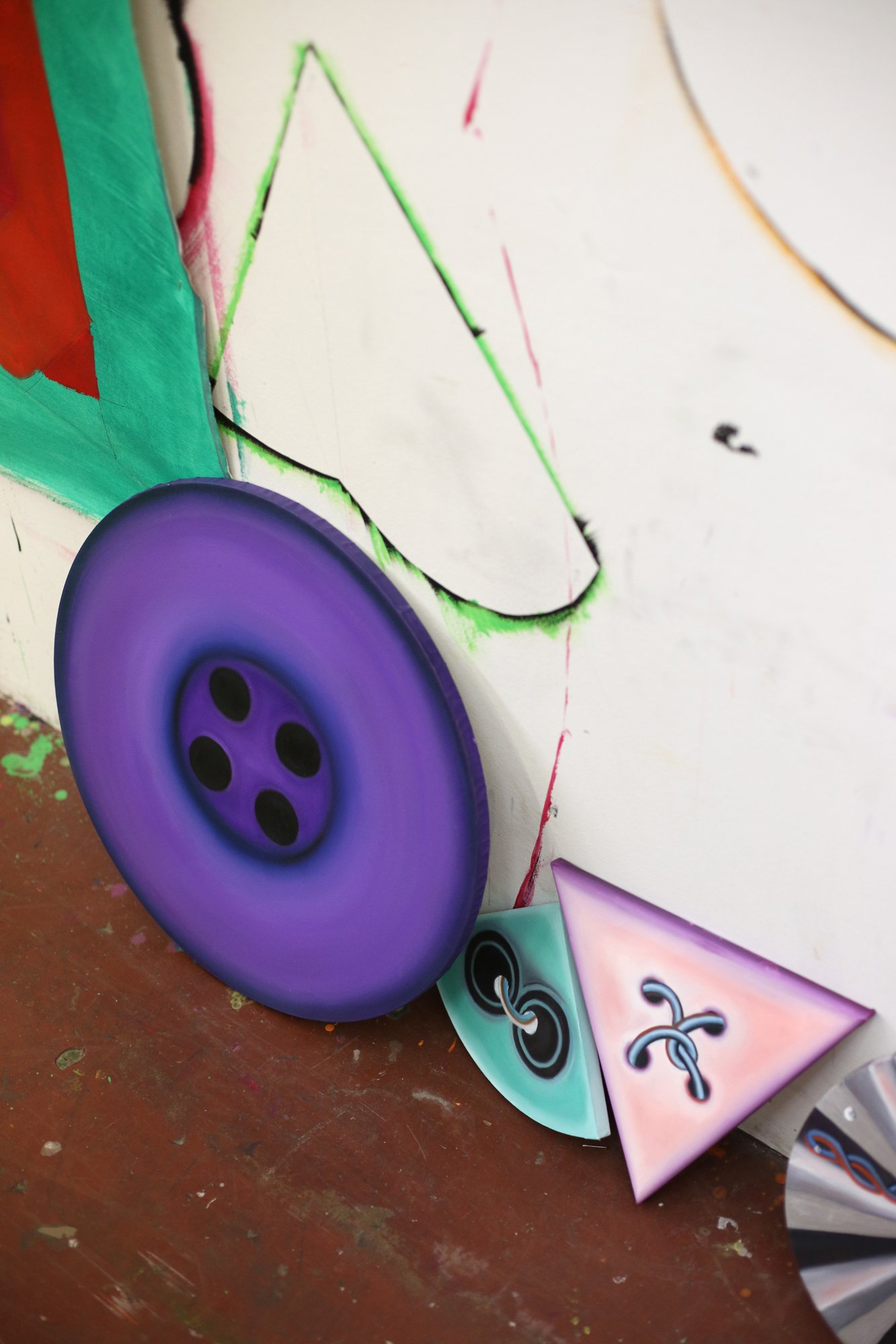 Various colorful round and triangular objects lean against a painted wall. One resembles a large purple button.