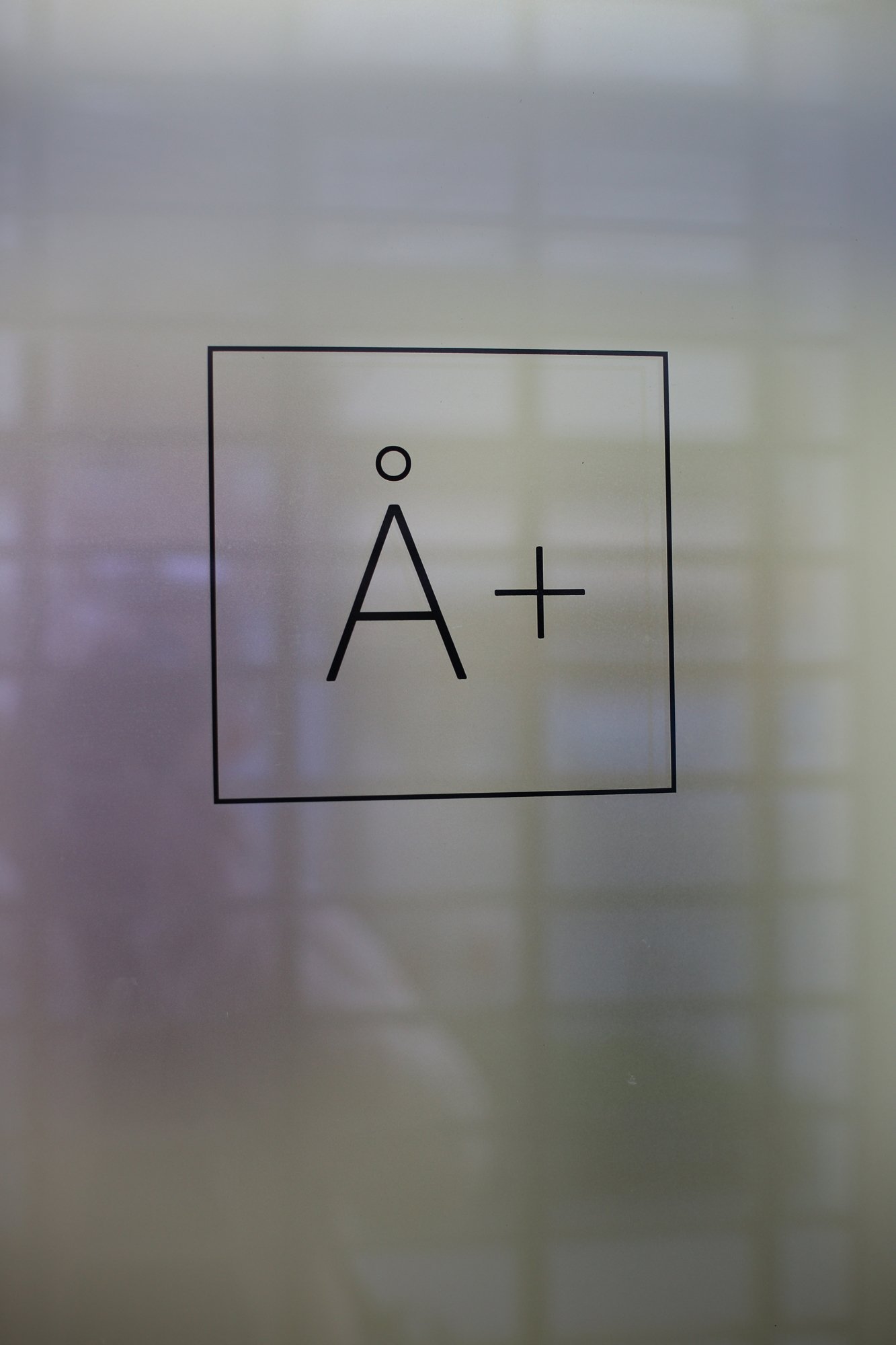Simple “Å+” logo inside a thin square frame on frosted glass.