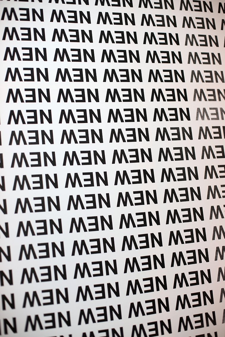 Black capital letters forming the word “MEN” appear in staggered rows on a white background, some of them upside down.