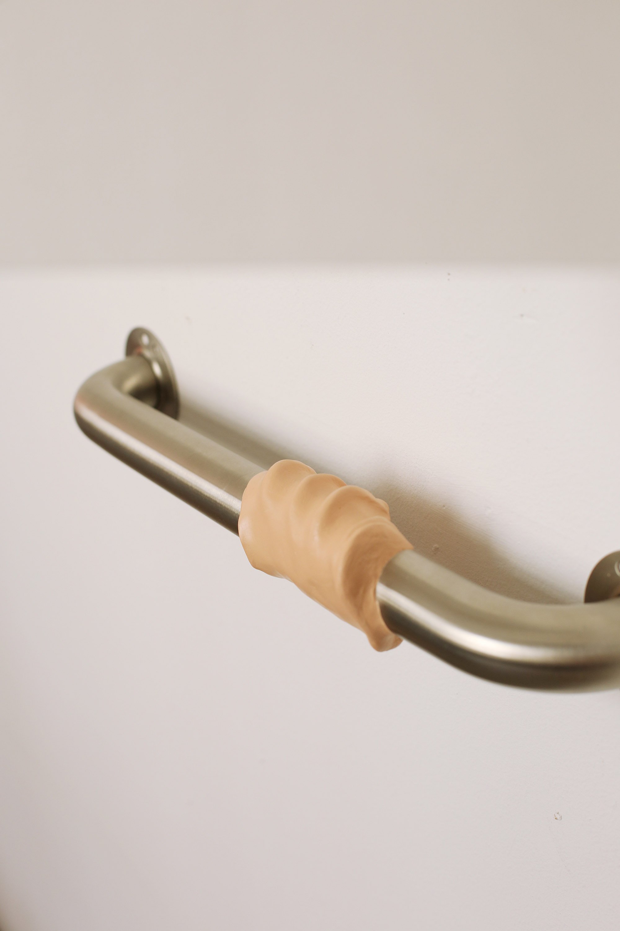 Metal handrail on a white wall, wrapped with a skin-coloured, moulded material shaped like a gripping hand.