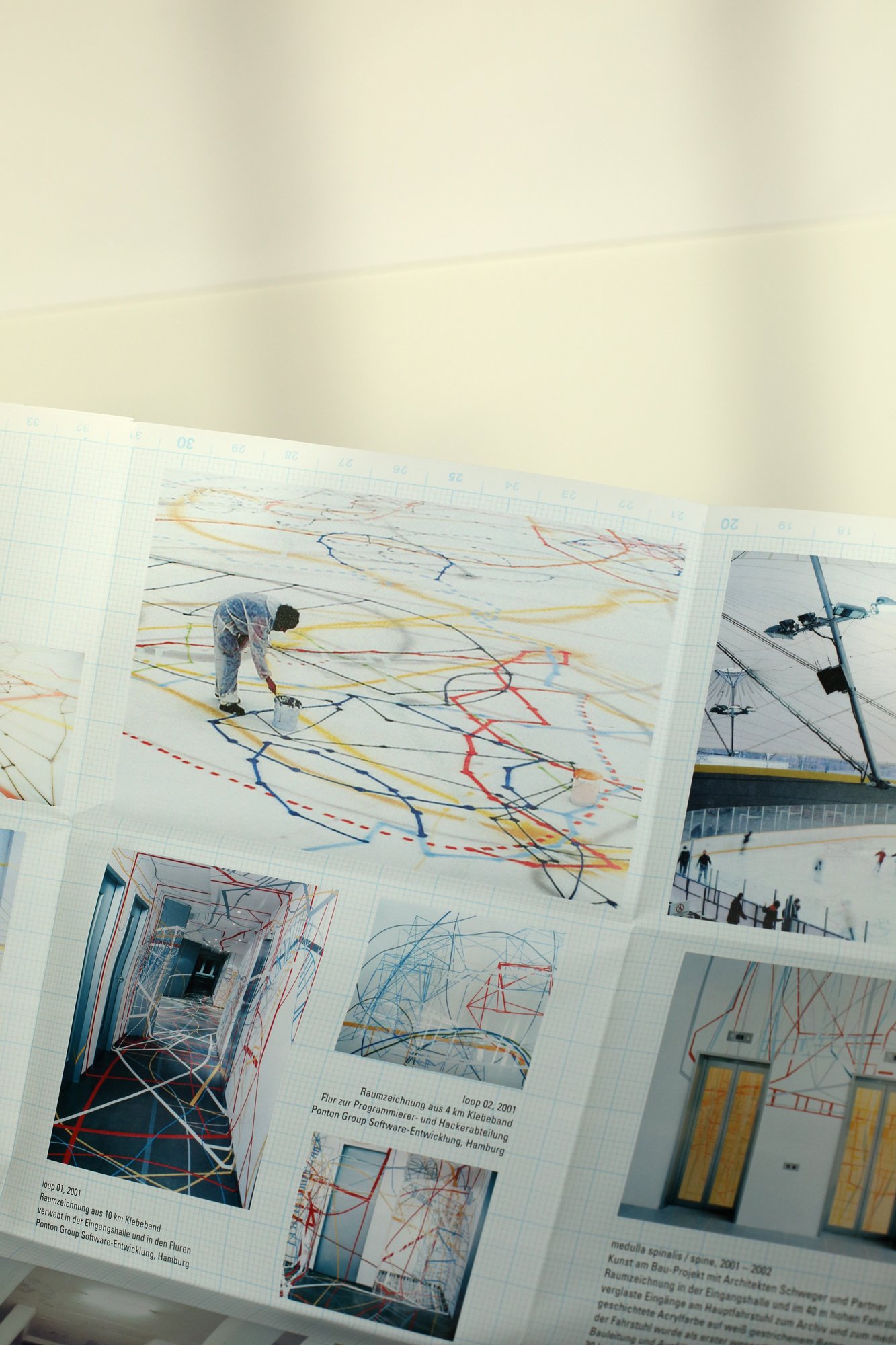An unfolded brochure displaying photographs of large-scale room drawings and installations made from colored lines.