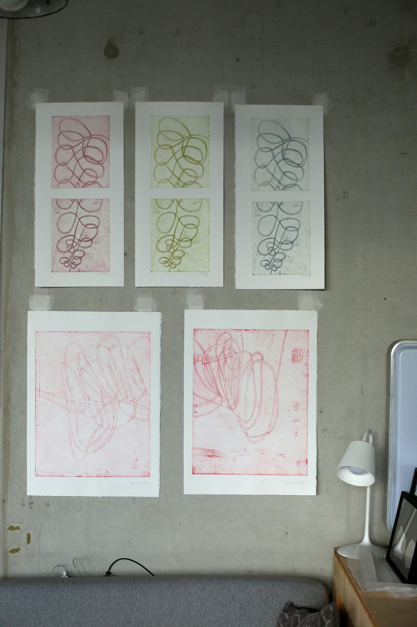 Several colorful print graphics with looping line patterns hang on a grey wall above a sofa.