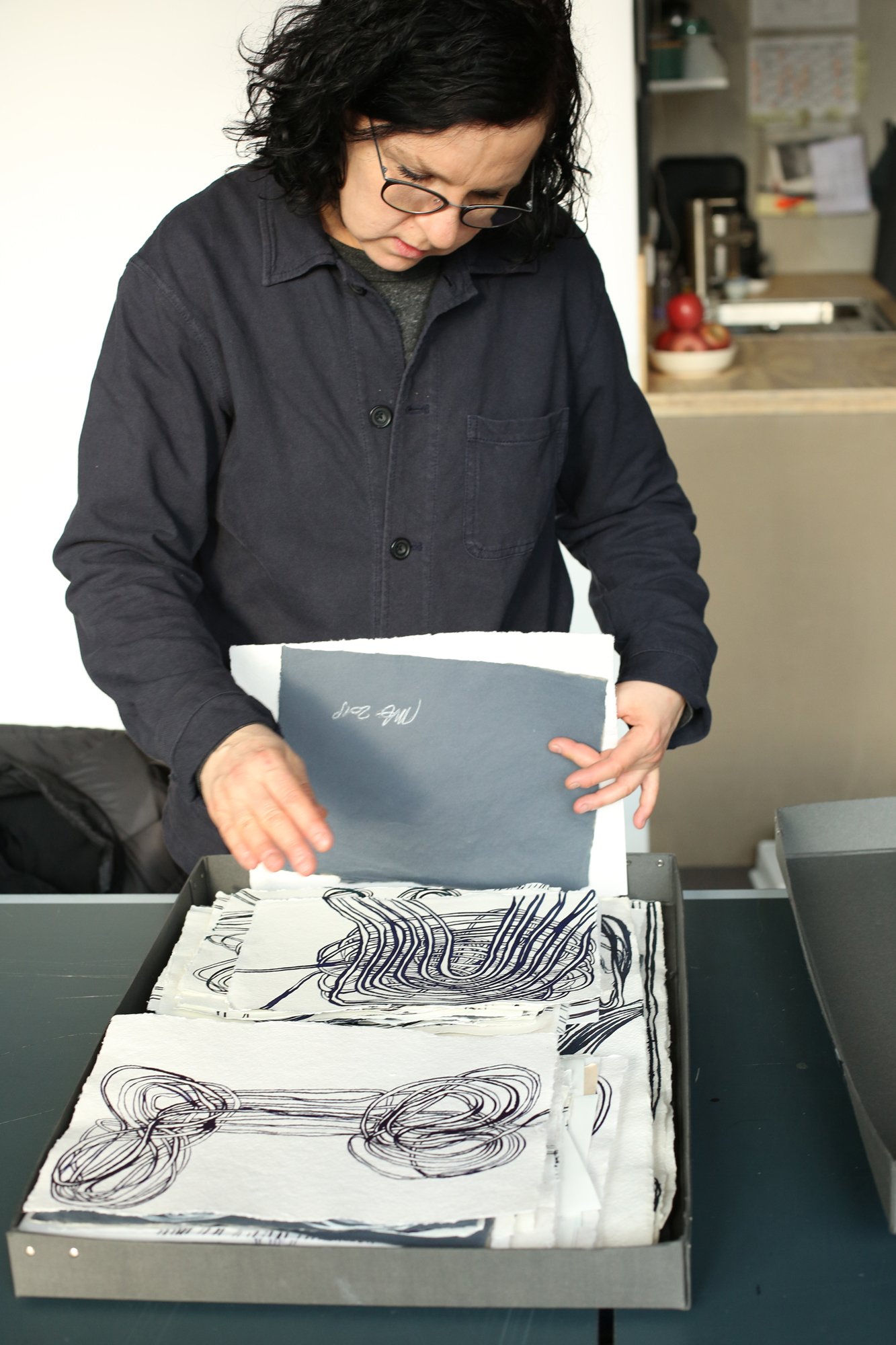 A person looks through and sorts a portfolio filled with graphic drawings featuring interwoven line patterns.