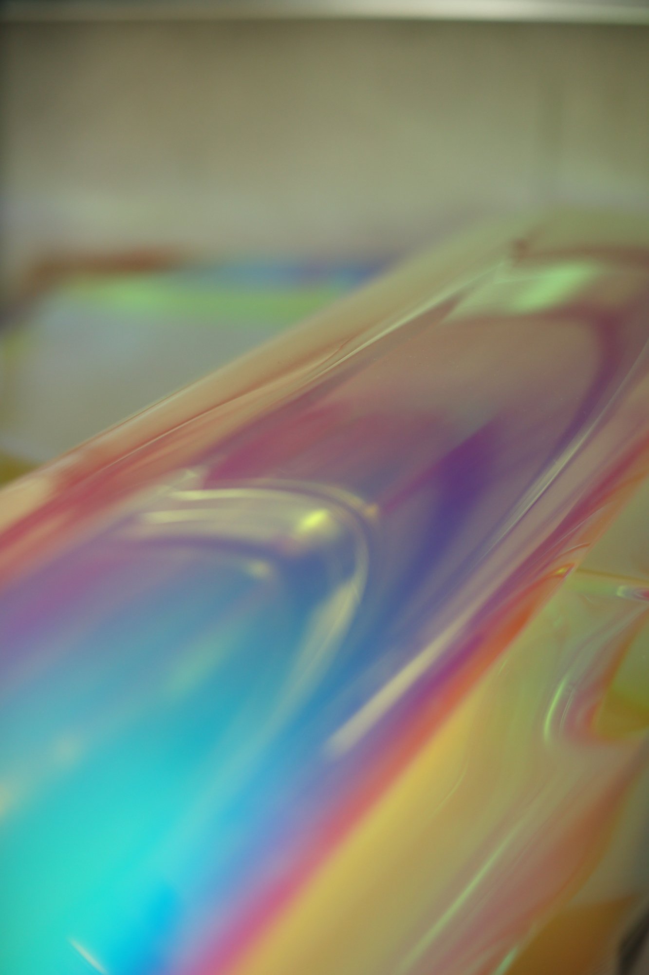 Close-up of a glossy, iridescent surface with soft color gradients in blue, pink, and yellow.