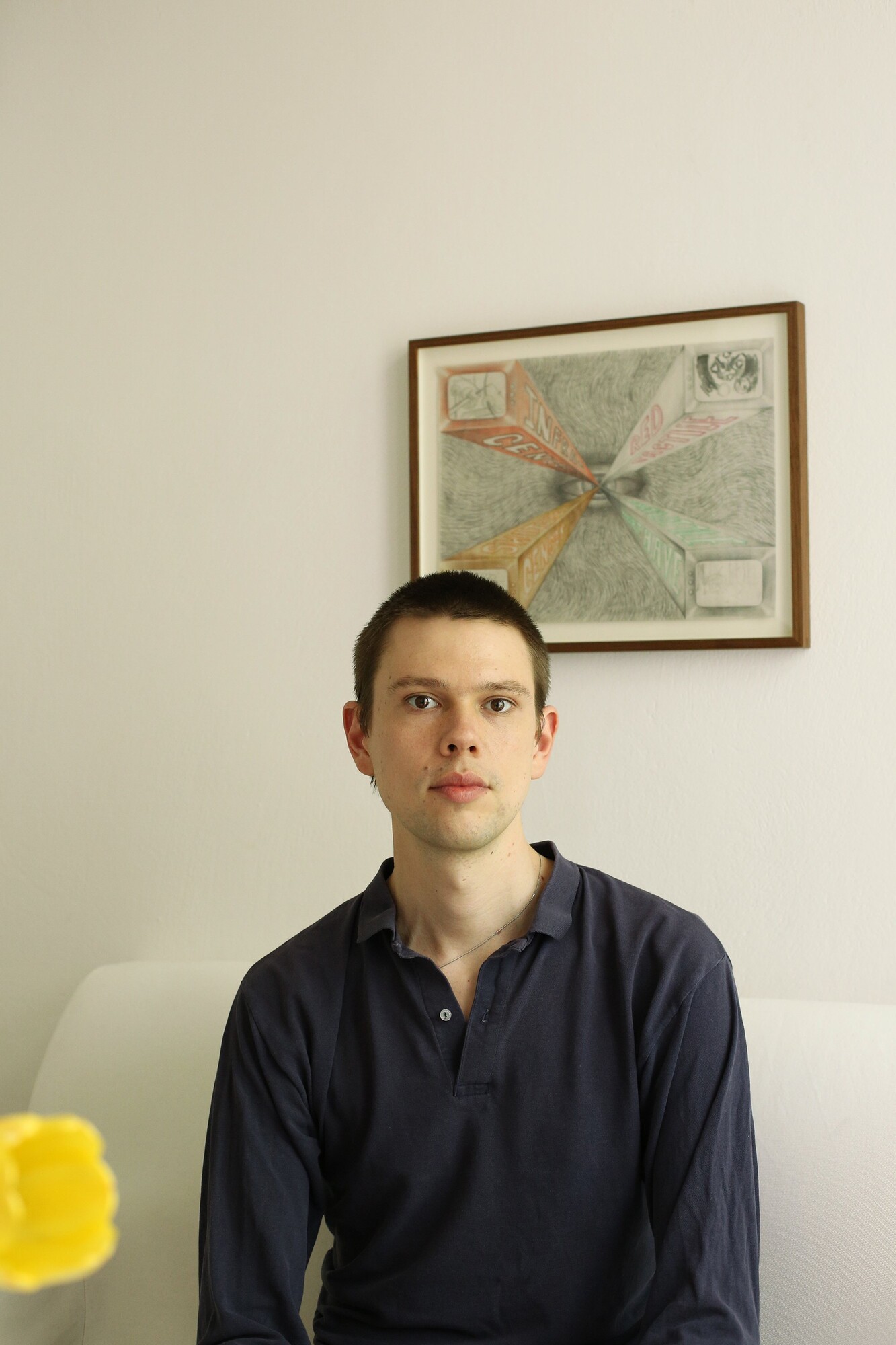 A person sits on a white sofa in front of a wall featuring a framed abstract drawing.
