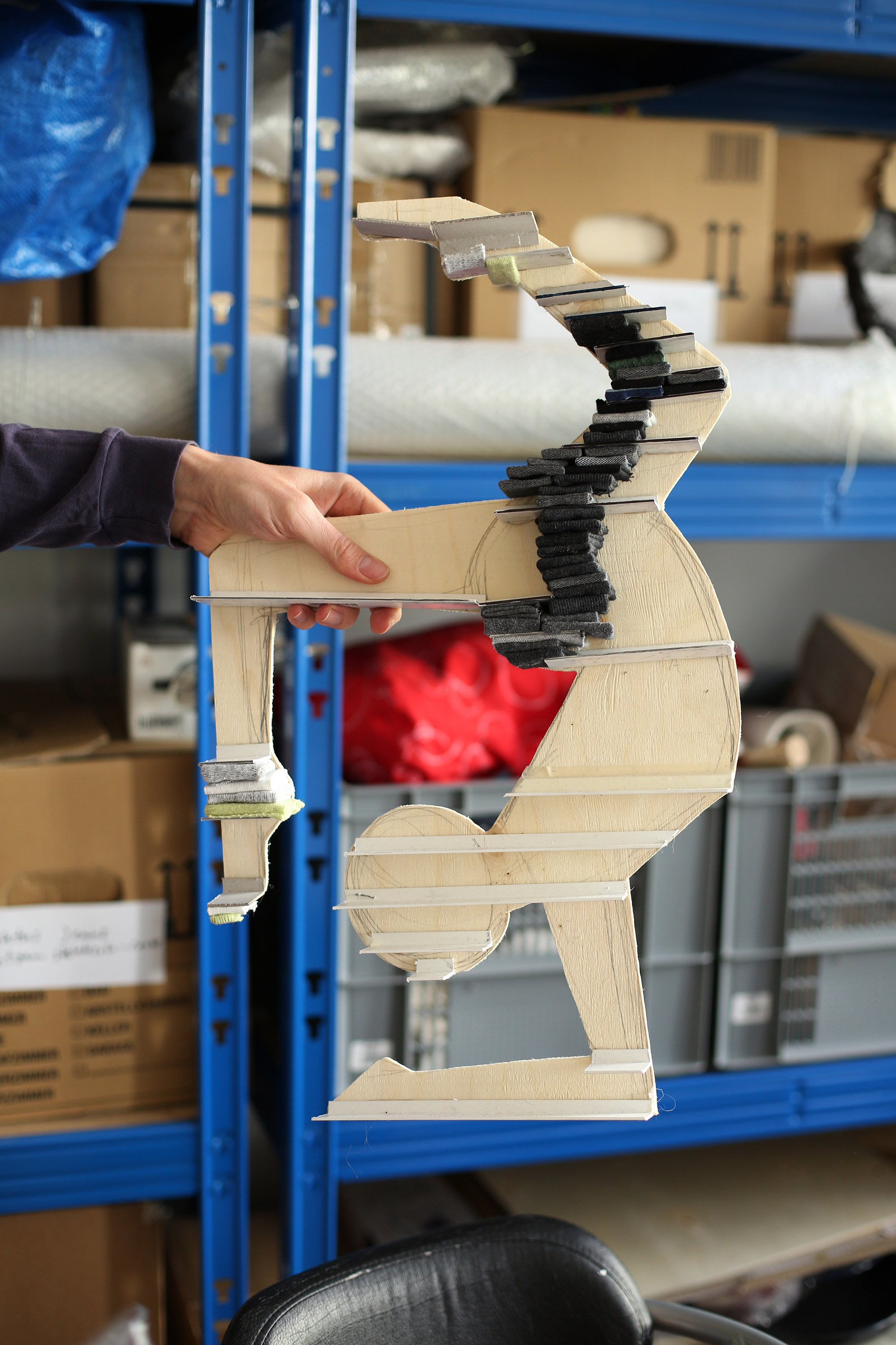Close-up of a contoured wooden model shaped like an acrobatic figure, held in one hand.