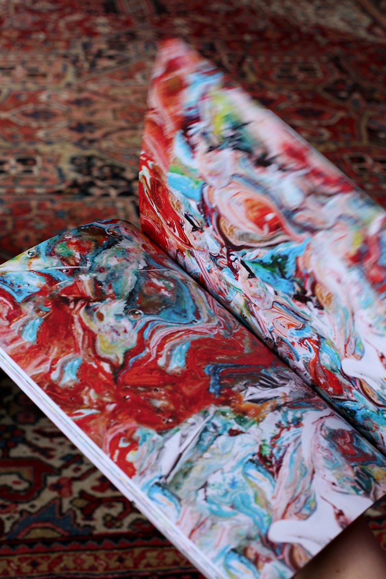 Close-up of an open book showing a brightly colored abstract image with red, blue, and white tones. The carpet underneath appears slightly out of focus.