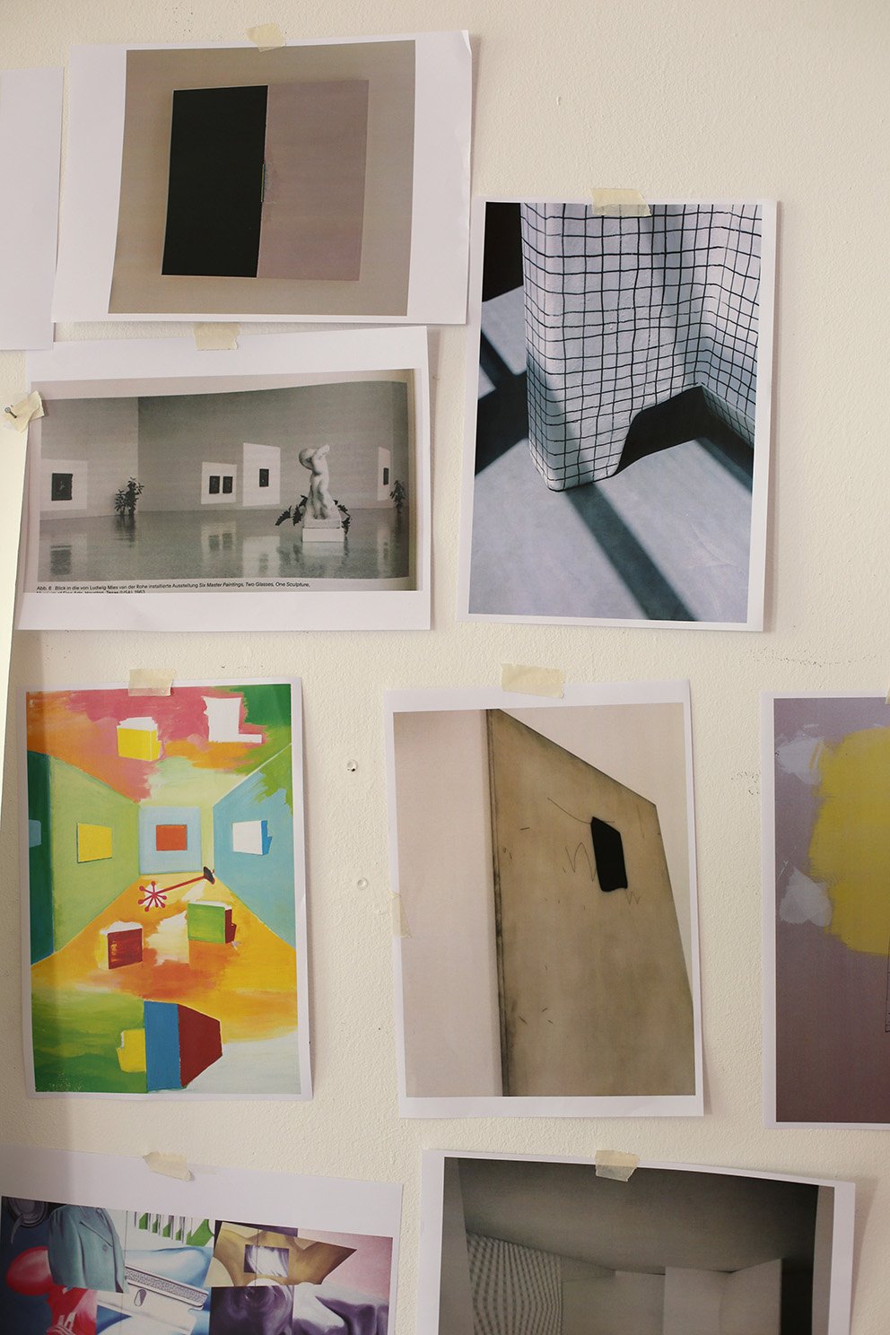 Several photographs and printed images are taped to a white wall, featuring various subjects including color compositions, architecture, and objects.