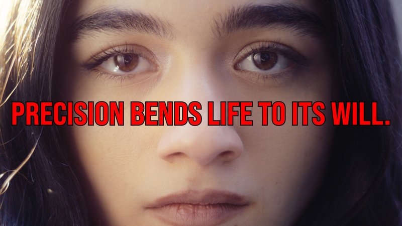 Nahaufnahme eines Gesichts mit ernstem Ausdruck. Über das Bild ist in großen roten Buchstaben der Satz „PRECISION BENDS LIFE TO ITS WILL.“ gelegt.