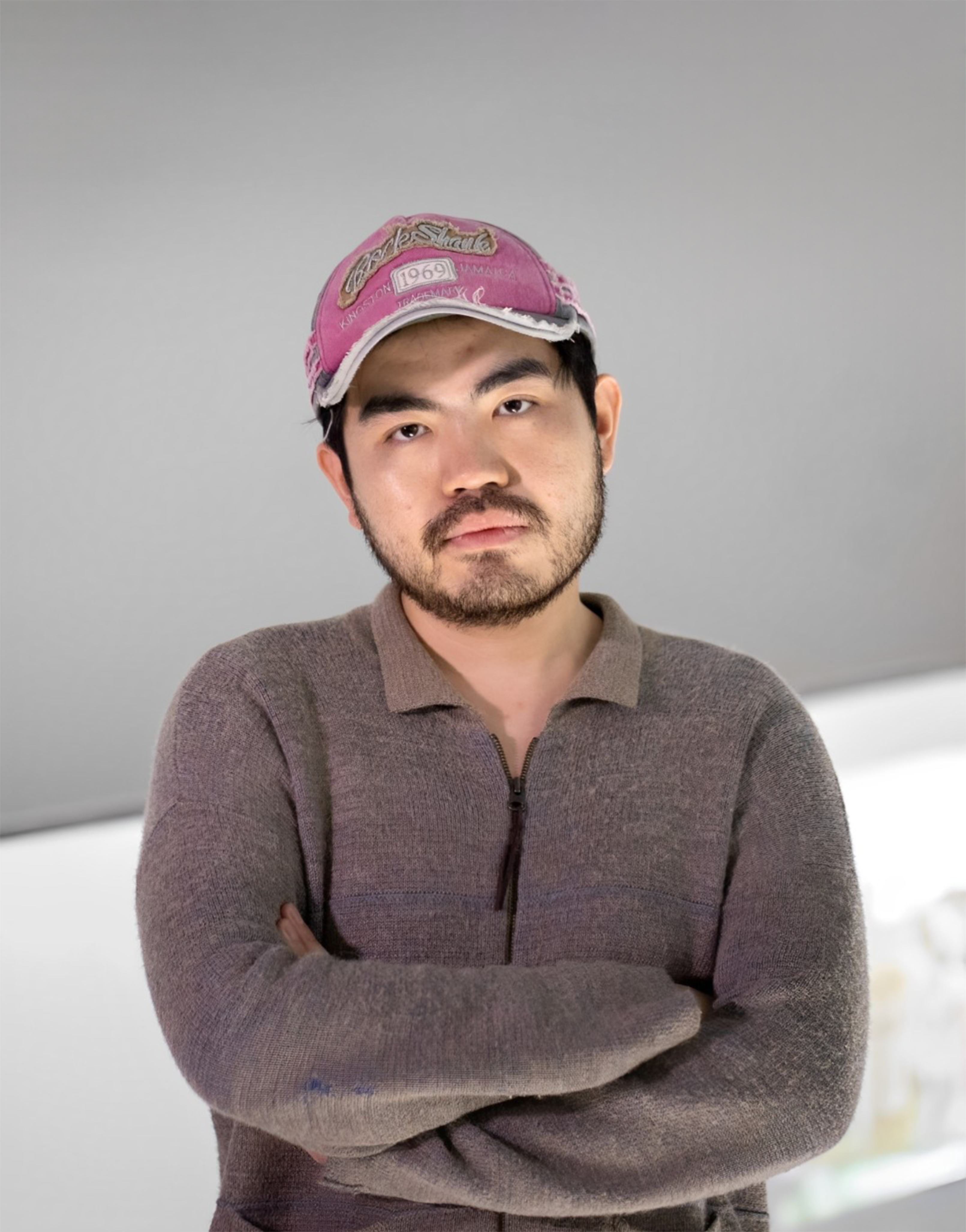 Mann blickt mit verschränkten Armen in die Kamera, er trägt eine Cappy und hat einen Dreitagebart