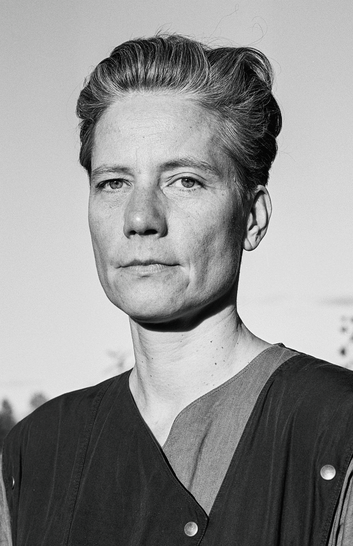 Eine Frau mit kurzen, nach hinten gekämmten Haaren blickt in die Kamera.