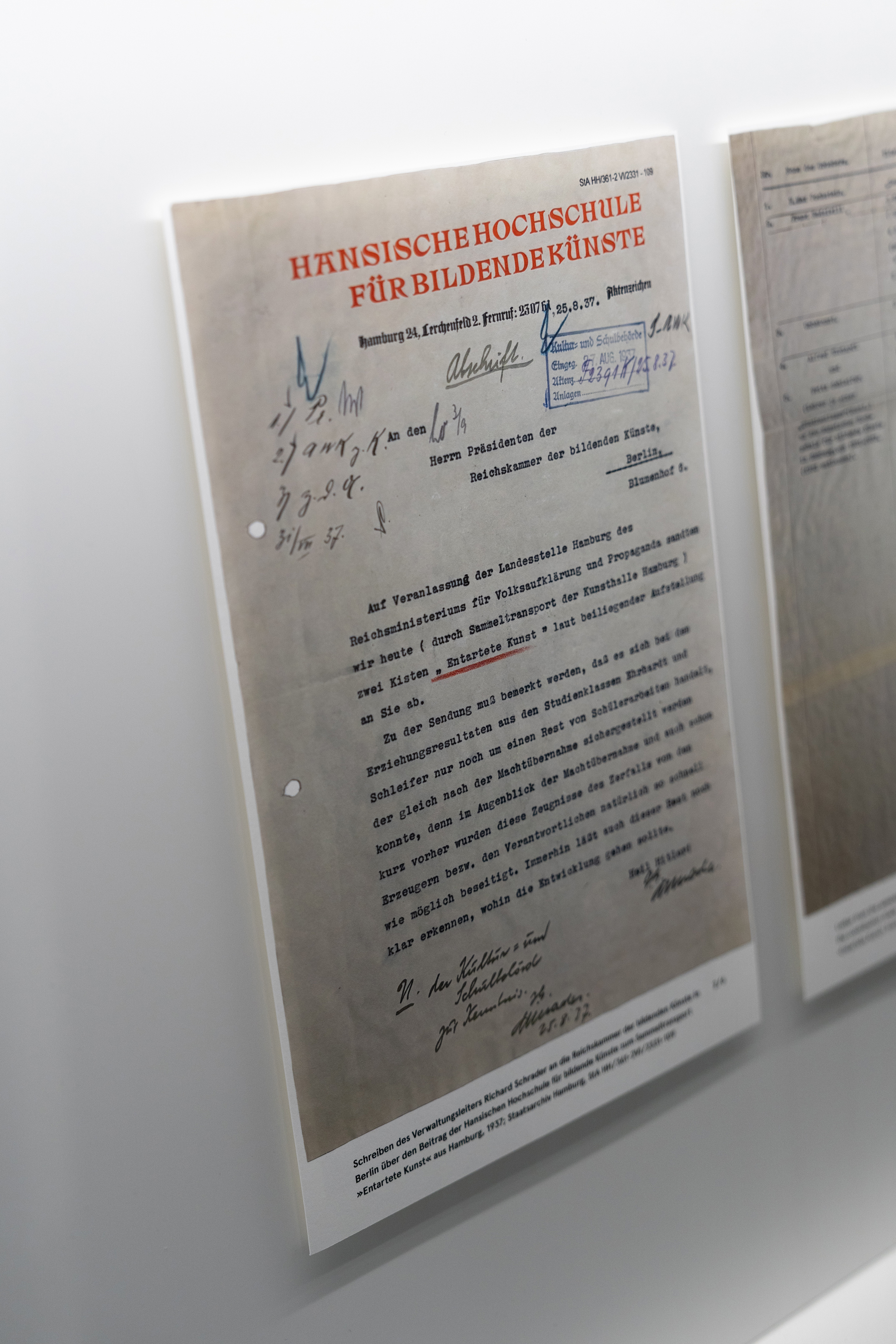 Nahaufnahme eines historischen Schreibens der Hansischen Hochschule für bildende Künste Hamburg aus dem Jahr 1937. Das Dokument mit rotem Briefkopf, handschriftlichen Vermerken und Stempeln ist Teil einer Ausstellung mit Archivmaterialien zur Geschichte der Hochschule im Nationalsozialismus.