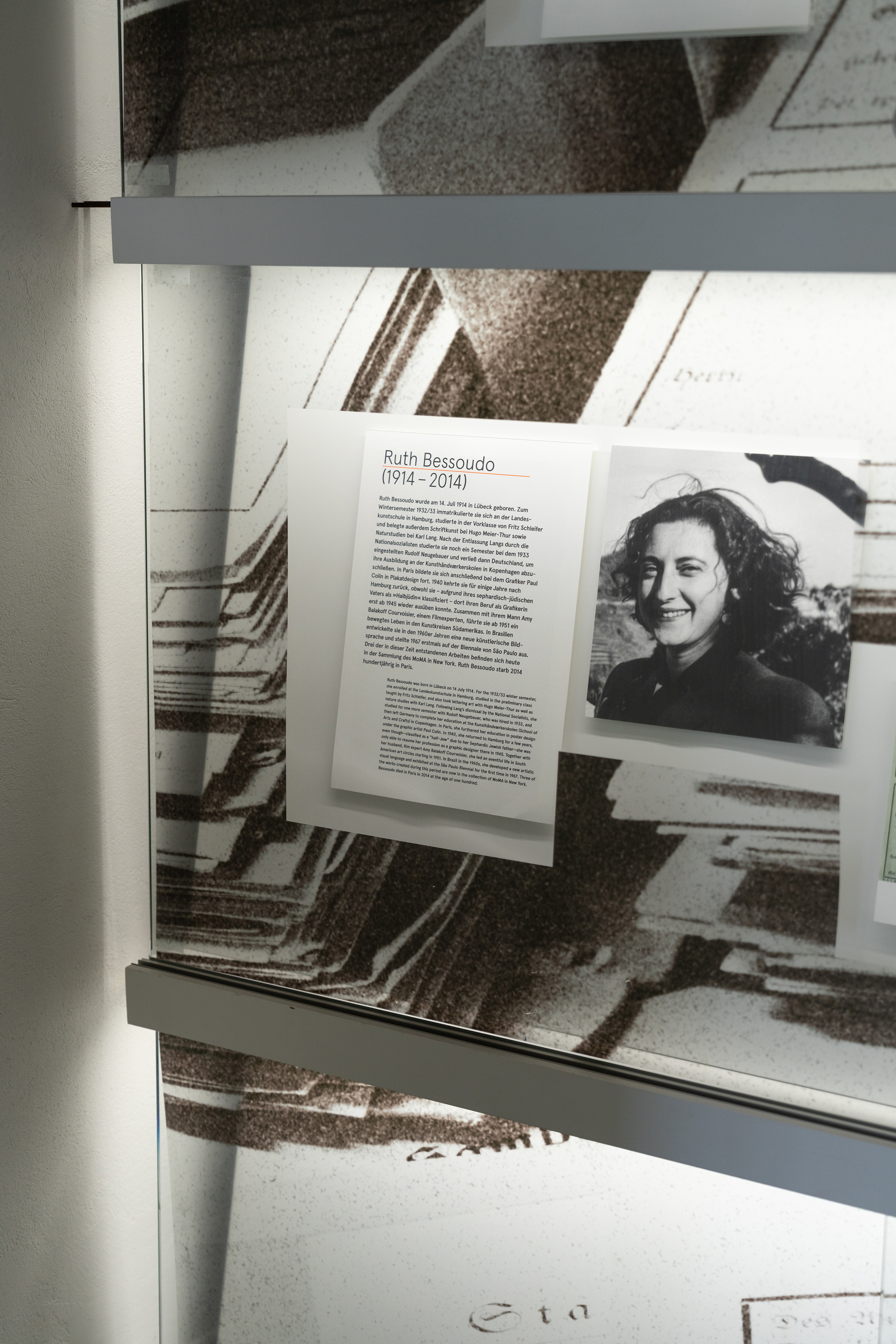 Detailansicht einer Vitrine mit Informationen zur Künstlerin Ruth Bessoudo (1914–2014). Neben einem historischen Porträt erläutert ein Begleittext ihren Lebensweg und ihre Verfolgung während der Zeit des Nationalsozialismus. Die Präsentation ist Teil einer Ausstellung mit Archivmaterialien zur Geschichte der Hochschule.