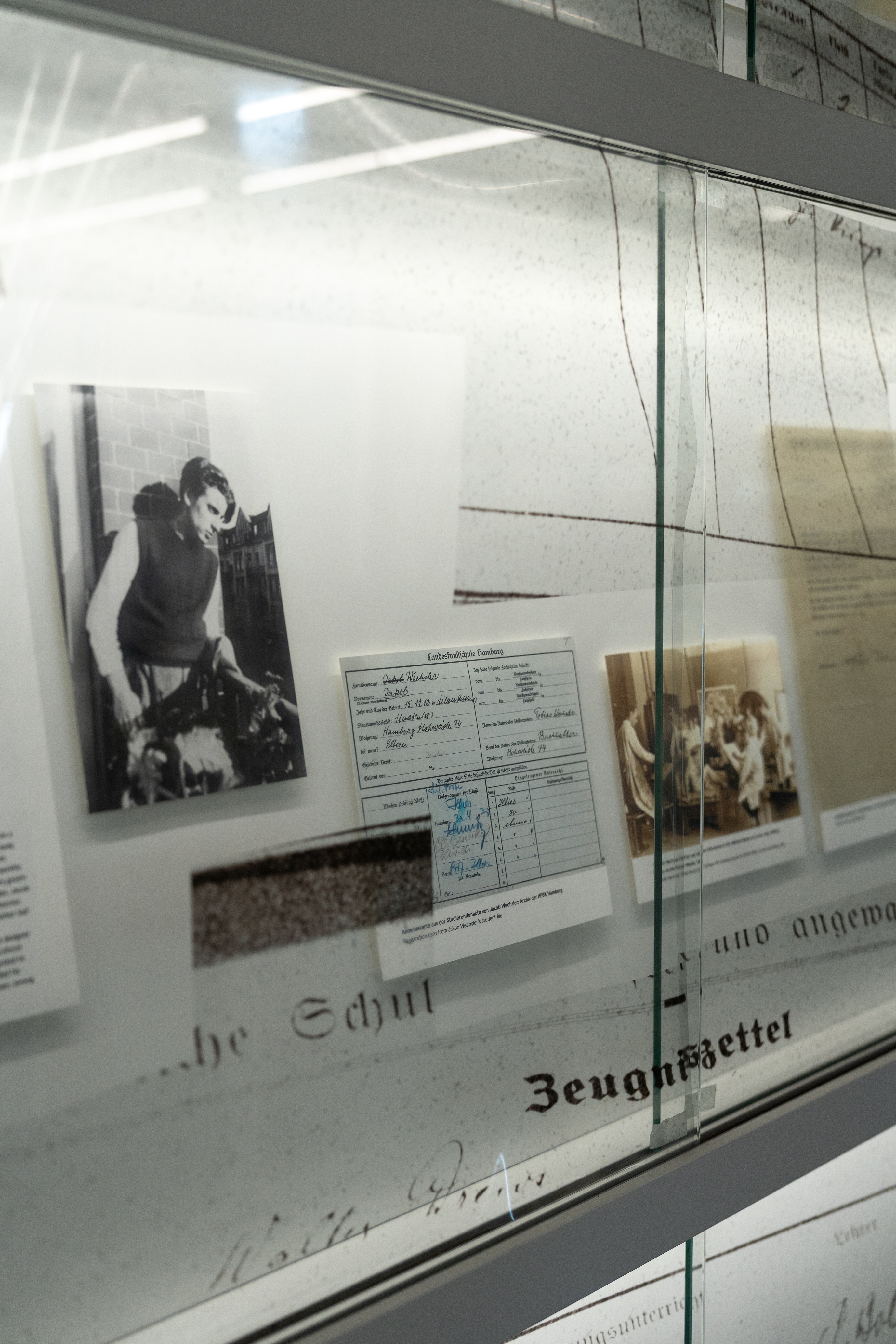 Blick in eine Vitrine der Bibliothek mit historischen Archivdokumenten und Fotografien zur Geschichte der Hochschule für bildende Künste Hamburg im Nationalsozialismus. Die Dokumente sind hinter Glas präsentiert und Teil einer Ausstellung im Bibliotheksmagazin.