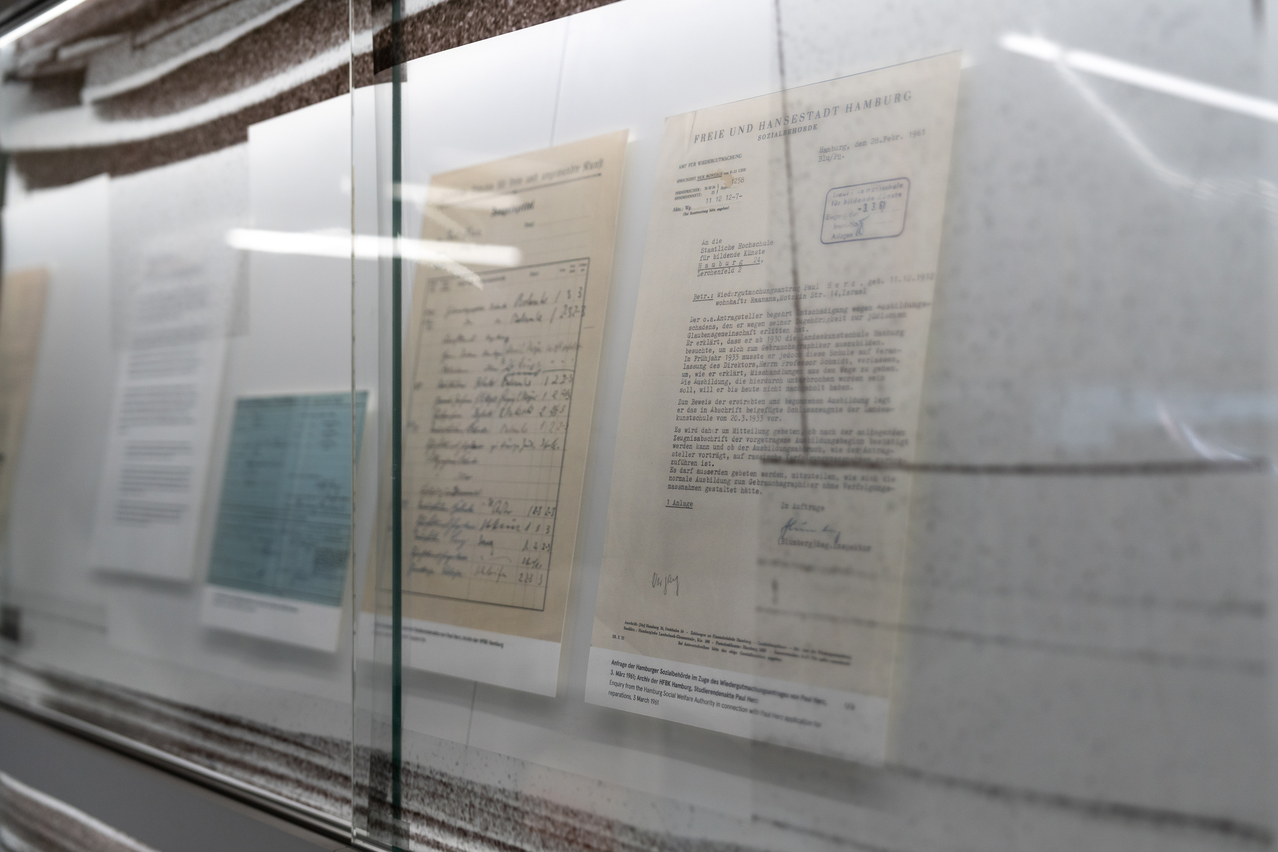 Blick in eine Vitrine der Bibliothek mit historischen Archivdokumenten und Fotografien zur Geschichte der Hochschule für bildende Künste Hamburg im Nationalsozialismus. Die Dokumente sind hinter Glas präsentiert und Teil einer Ausstellung im Bibliotheksmagazin.