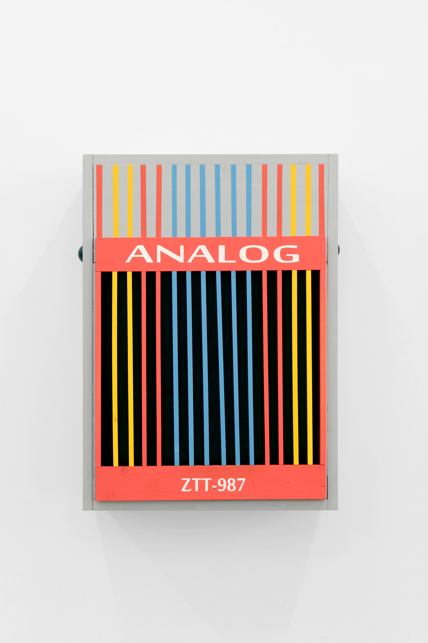 Auf einem grauen viereckigen Kasten mit einer Aufschrift sind Striche in Gelb, Rot, Blau zu sehen.