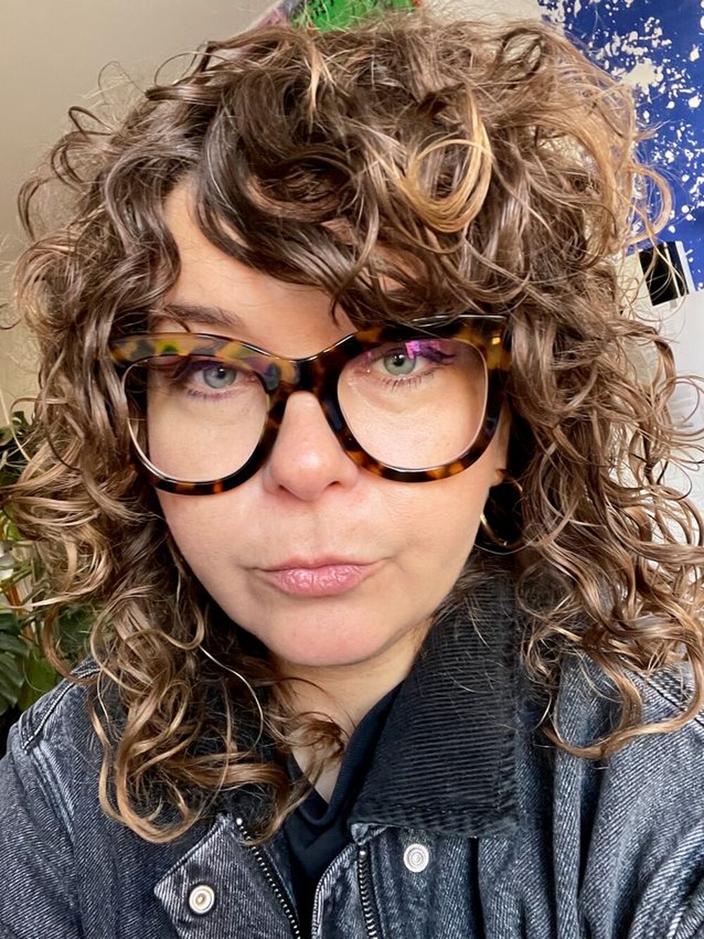 Eine Frau mit großer Brille mit Leoparden-Print und lockigen dunkelblonden Haaren schaut in die Kamera.