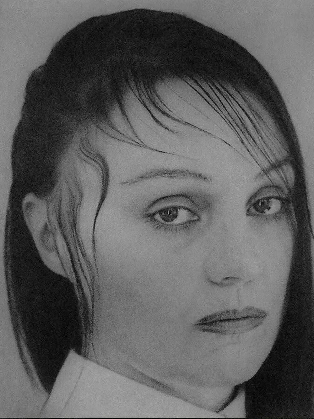 Auf einem schwarz-weiß Portrait blickt eine Frau mit dunklen Haaren, die ihr teilweise strähnenweise ins Gesicht gekämmt sind, seitlich in die Kamera.