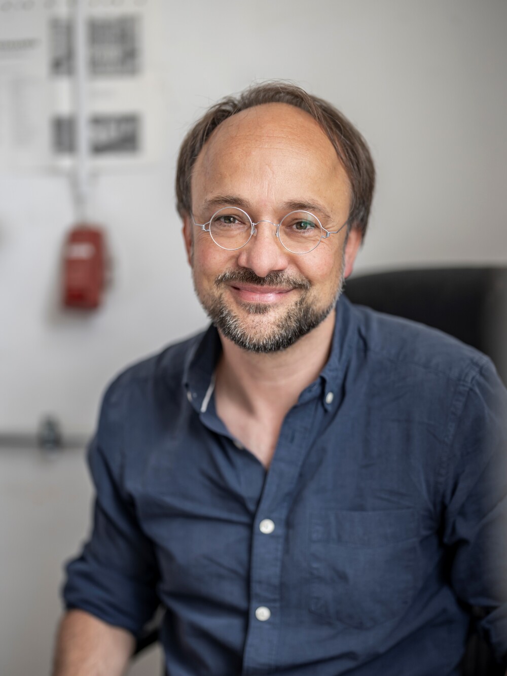 Ein Mann mit runder Brille mit dünnem, silbernen Metallgestell lächelt in die Kamera. Er hat dunkelblonde Haare und einen Dreitagebart.