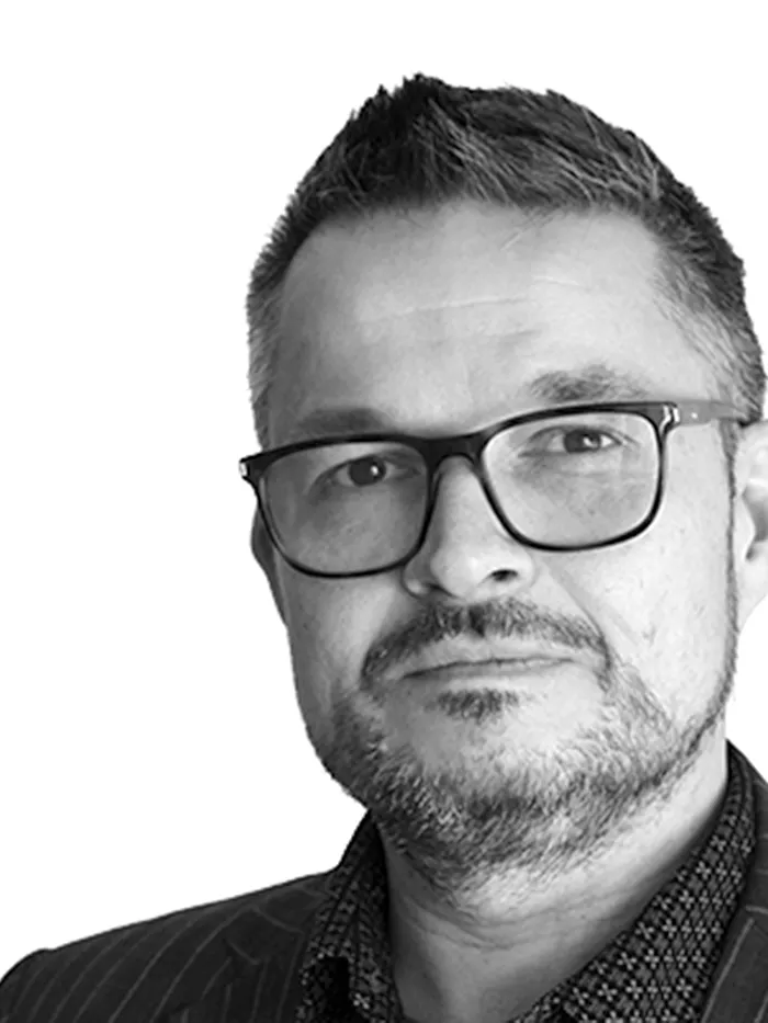 Black-and-white portrait of a man wearing glasses with short hair, photographed against a light background, with the head partially cropped on the right side.