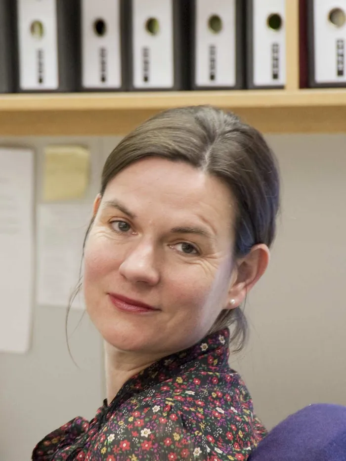 Portrait of a woman in an office, turning in her chair to look at the camera; shelves with binders in the background.